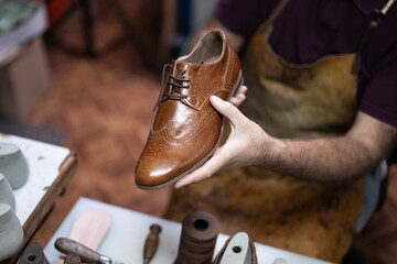 Cobbler presents a polished brown leather wingtip dress shoe in a craftsman's workshop