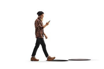 Young man in checkered shirt and jeans using a mobile phone and walking toward open manhole