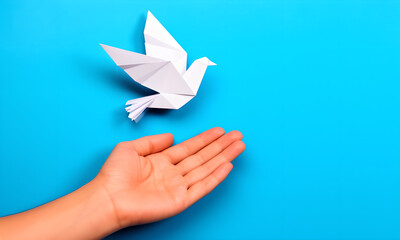 Open human hand reaching towards a white origami dove on vibrant blue background.