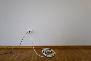 Electrical cords plugged into the wall outlet. Minimalist interior with cables on a wooden floor. Simple home power connection scene. Household electricity setup and energy consumption concept.