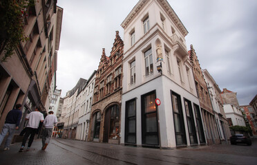 Narrow street in a historic European city with traditional buildings and pedestrians walking along the old town roadway.
