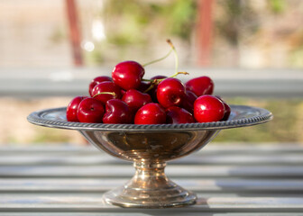 Fresh cherries in a silver bowl on a wooden table outdoors