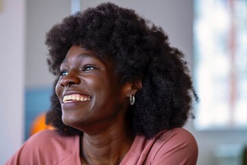 A joyful young woman with an afro hairstyle and nose ring is captured mid-laugh while looking at...