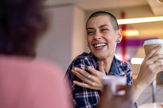 Two women laughing heartily together, one holding a coffee cup