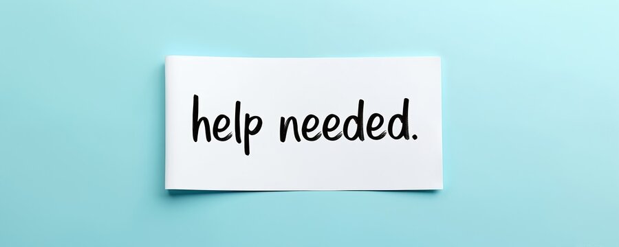 White paper card shows text help needed. Simple message written with black marker ink. Plain background shows light blue color. This implies request for aid or support.