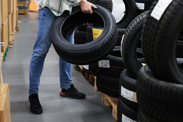 Man holding a new car tire in an auto parts store warehouse, choosing winter or summer tyres for his vehicle. © Kyrylo