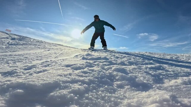LENS FLARE, CLOSE UP, LOW ANGLE VIEW, SLOW MOTION: Snowboarder crashes and plows into snow while riding down the ski slope. Sparkling ice crystals fly through the air as he tries to stop while sliding