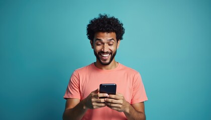 Young man looks at his smartphone with a wide, surprised smile. He laughs enthusiastically at something on his phone screen against a blue background.