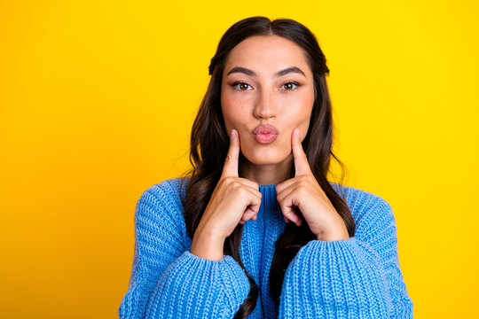 Young mixed race woman in blue sweater making kissy face against bright yellow background for lifestyle fashion and casual studio shot