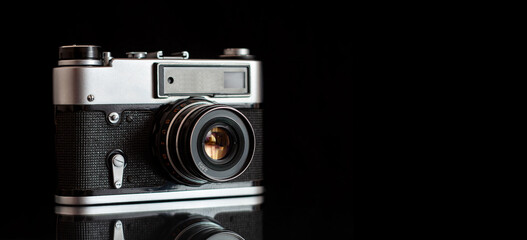 Vintage film camera on a black reflective surface against a dark back