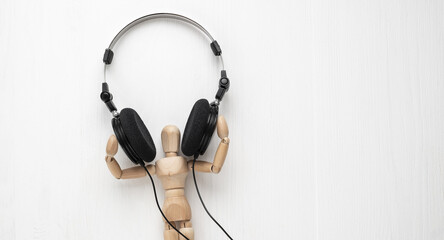 Wooden mannequin wearing large black headphones on a white textured back