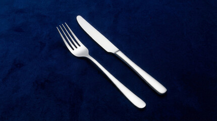 Elegant stainless steel fork and knife set on a dark blue velvet background
