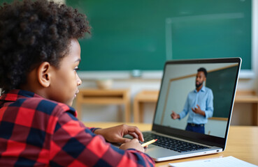 African american boy learns online via laptop computer. Teacher speaks on screen. Child studies remotely in classroom. Education tech connects pupil instructor. Remote learning, digital lesson.
