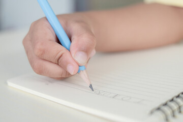 Close up to a child hand writing something on the paper with pencil