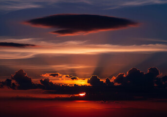 Beautiful sunset with sunbeams piercing through dark clouds over a calm ocean, evoking a sense of peace and natural wonder