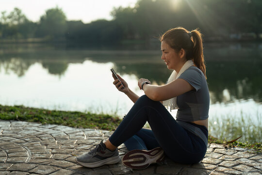 Sport young woman using mobile and looking at smartwatch on her wrist, tracking fitness activity during training outdoors