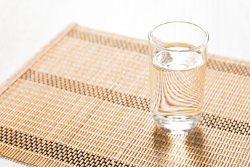 和風マットの上に置かれたグラスの水 Glass of water on a Japanese-style placemat in bright light