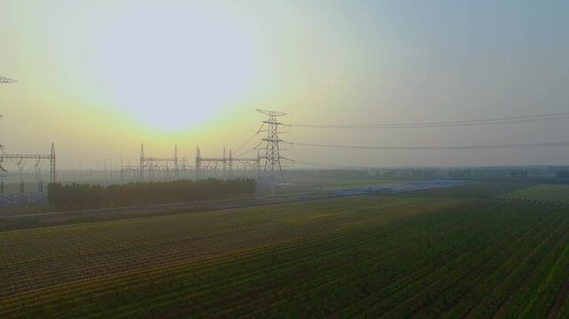 High Voltage Power Tower and Transmission Lines Over Farmland at Sunrise
