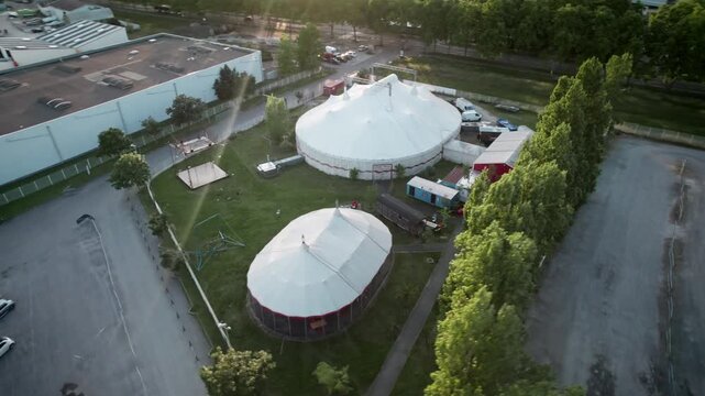 A circus tent is set up in a field with a large building in the background. With drone movement, panoramical in the sunset. Bordeaux, France.