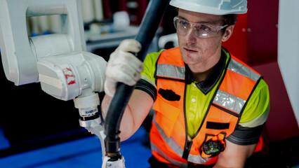 A male engineer in a hard hat holds a laptop while inspecting electrical wires. He is a specialist...
