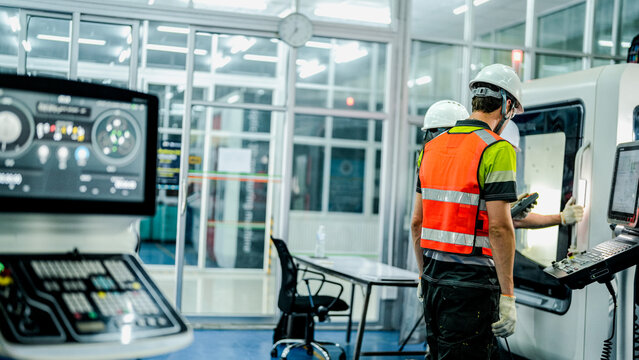 Three engineers program an industrial robot or 5-axis CNC machine using an AI interface. The team manufactures advanced microchips or high-tech components in a smart factory.