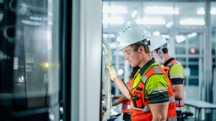 A team of engineers in hard hats and safety vests operates a high-tech industrial machine. The man in the foreground programs the advanced equipment in a smart factory.