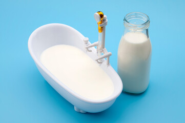 Milk Bath Skincare Concept with Mini Bathtub Filled With Milk and Glass Bottle on Blue Background
