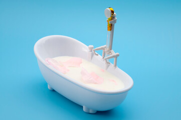 Milk Bath Spa Concept with Rose Petals Floating in Mini Bathtub on Blue Background