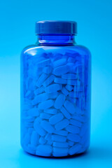 Medicine, pharmaceutical industry and headache medication concept with white pills in transparent plastic bottle isolated on blue background