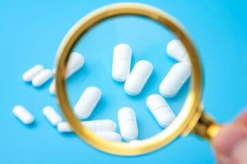 Laboratory investigation, medication inspection and pharmaceutical industry review with scientist using magnifying glass to zoom in and examine many prescription drugs isolated on blue background