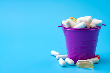 Excessive supplementation, wellness and wellbeing concept with many mixed vitamins and supplements in a metal bucket isolated on blue background with copy space