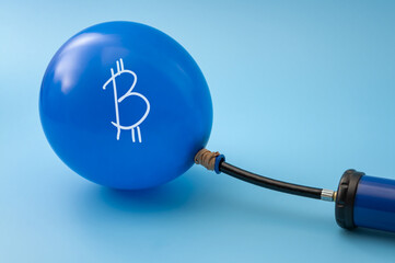 Inflating Bitcoin Bubble Concept with Hand Pump and Cryptocurrency Balloon on Blue Background