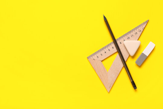 Triangle ruler with pencil and different rubber erasers on yellow background