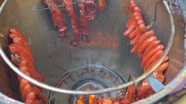 A high-angle shot captures the traditional vertical roasting process of Char Siu and sausages inside a large charcoal barrel oven.