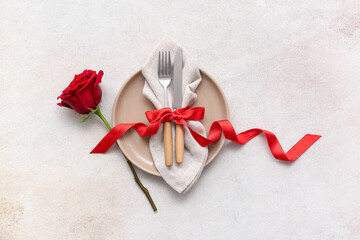 Table setting for Valentine's Day with cutlery, ribbon and rose flower on light background
