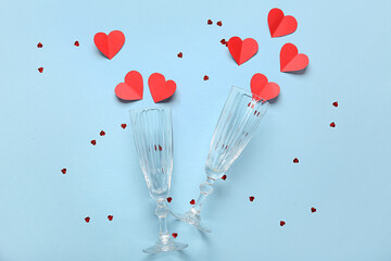 Champagne glasses with red paper hearts and confetti on blue background. Valentine's Day celebration