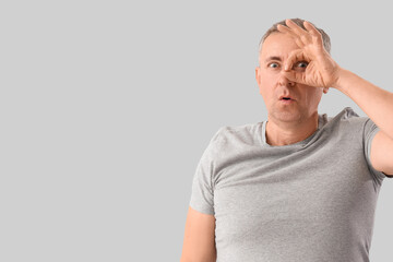Surprised mature man looking through imaginary telescope on light background