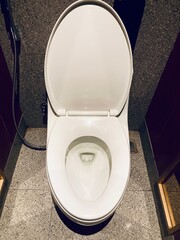 modern white ceramic toilet with open lid in a public restroom with gray stone floor