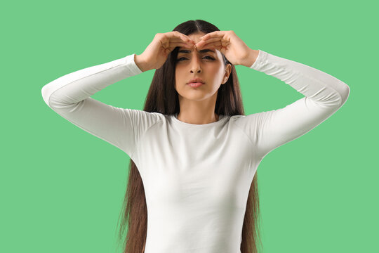 Beautiful young woman looking far away with hands over head on green background - Powered by Adobe
