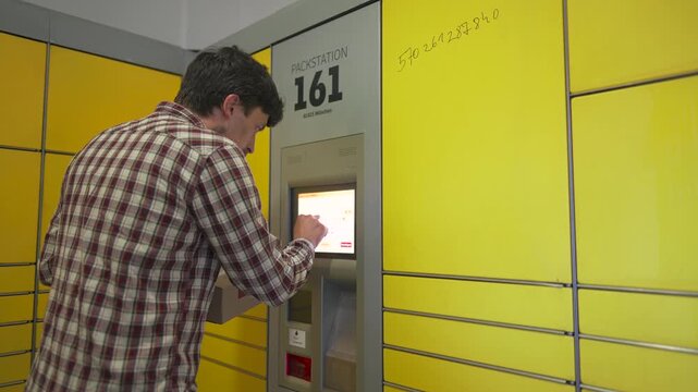 Yellow self-service postal terminal. Man sending parcel. Parcel pick up point, contactless self service post terminal, parcel delivery. Man putting box to parcel machine. Deposit for package storage