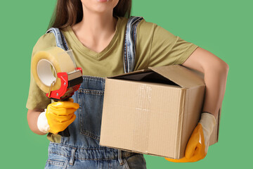 Young woman with adhesive tape dispenser and cardboard box on green background, closeup