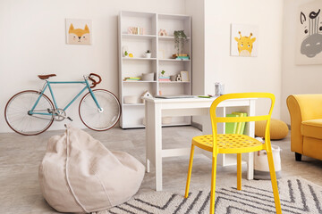 Interior of room with children's workplace, shelving units, yellow sofa, bicycle and beanbag chair