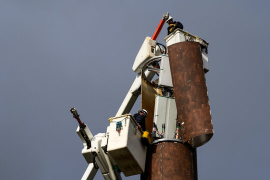 Wireless communications cell site with antenna cover open, boom arm lifting new antennas to crew, workman in lift bucket upgrading wireless equipment to 5G technology, stormy winter day
