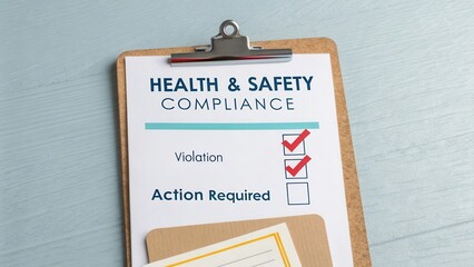 Health and Safety Compliance Checklist with Checked Violation and Action Required Sections on Wooden Desk Surface