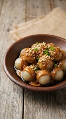 Fototapeta premium A bowl of small round dumplings topped with sesame seeds and herbs on a wooden table