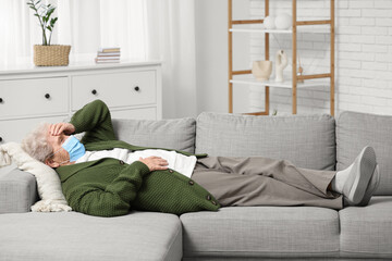 Sick elderly woman in medical mask lying on sofa in living room