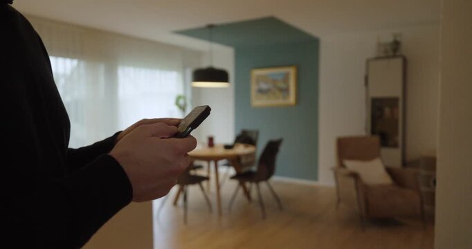 Lifestyle shot of a person using a smartphone to control a lamp in the background&mdash;ideal for smart home lighting, AI automation, remote control, and modern connected living.
