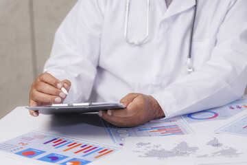 Doctor in white coat reviews medical charts and graphs on tablet, surrounded by printed data sheets, indicating focus on healthcare analytics
