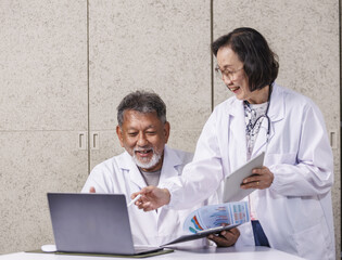 Two doctors in white coats are discussing medical data on laptop and tablet, smiling and collaborating in clinical setting. atmosphere is professional and positive