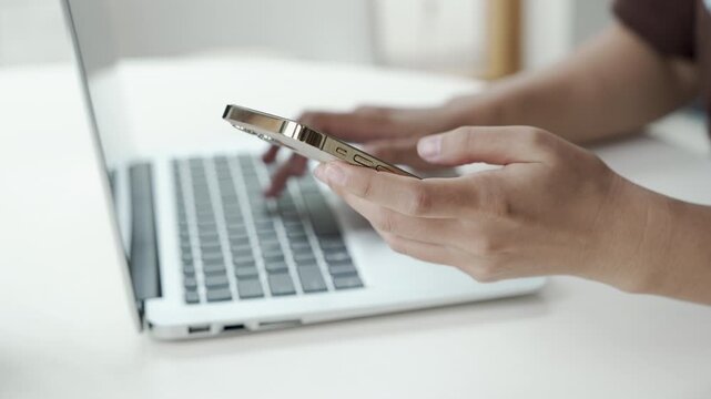 Close up man hands using smartphone and laptop computer for two factor authentication or multitasking. Business person working at office desk. Concept of digital technology, connection and finance